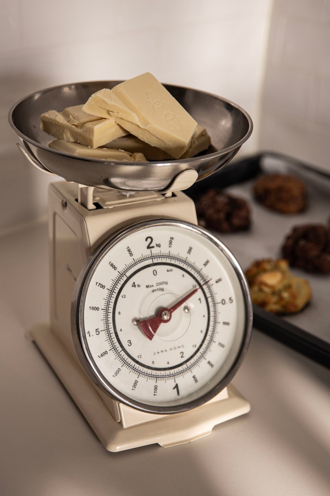 Pieces of white chocolate in a food balance with baked cookies on the background
